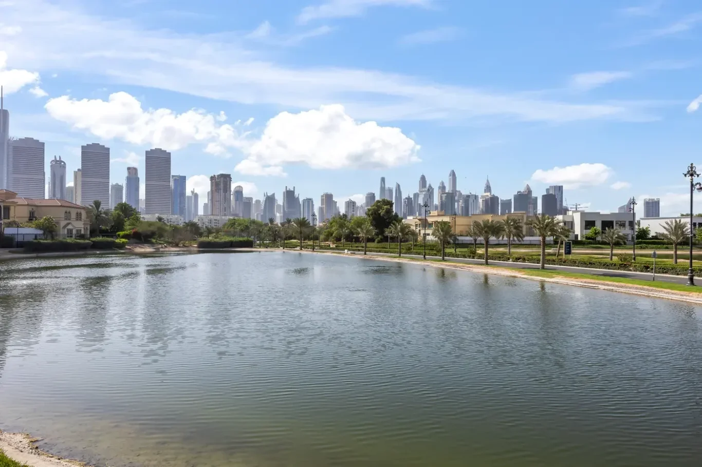 City skyline across a calm lake, with a palm-lined promenade in the foreground.
