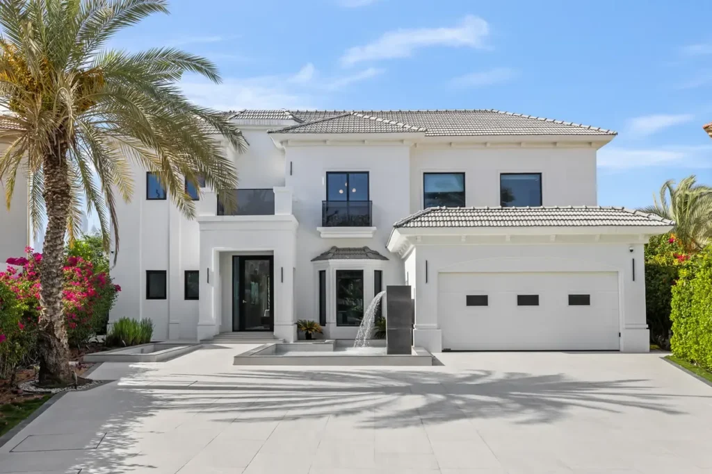 Modern white two-story house with a tiled roof, palm trees, and a small fountain near the front steps.