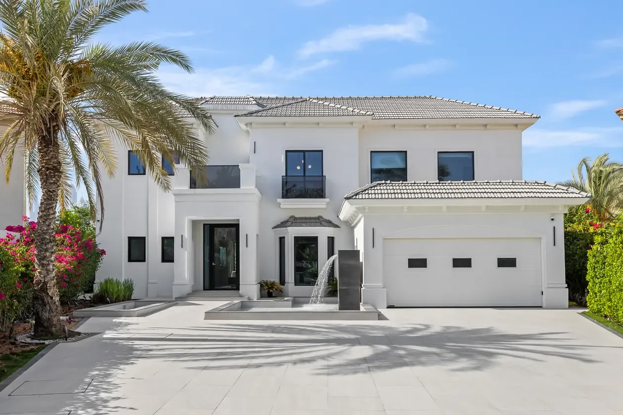 Modern white two-story house with a tiled roof, palm trees, and a small fountain near the front steps.