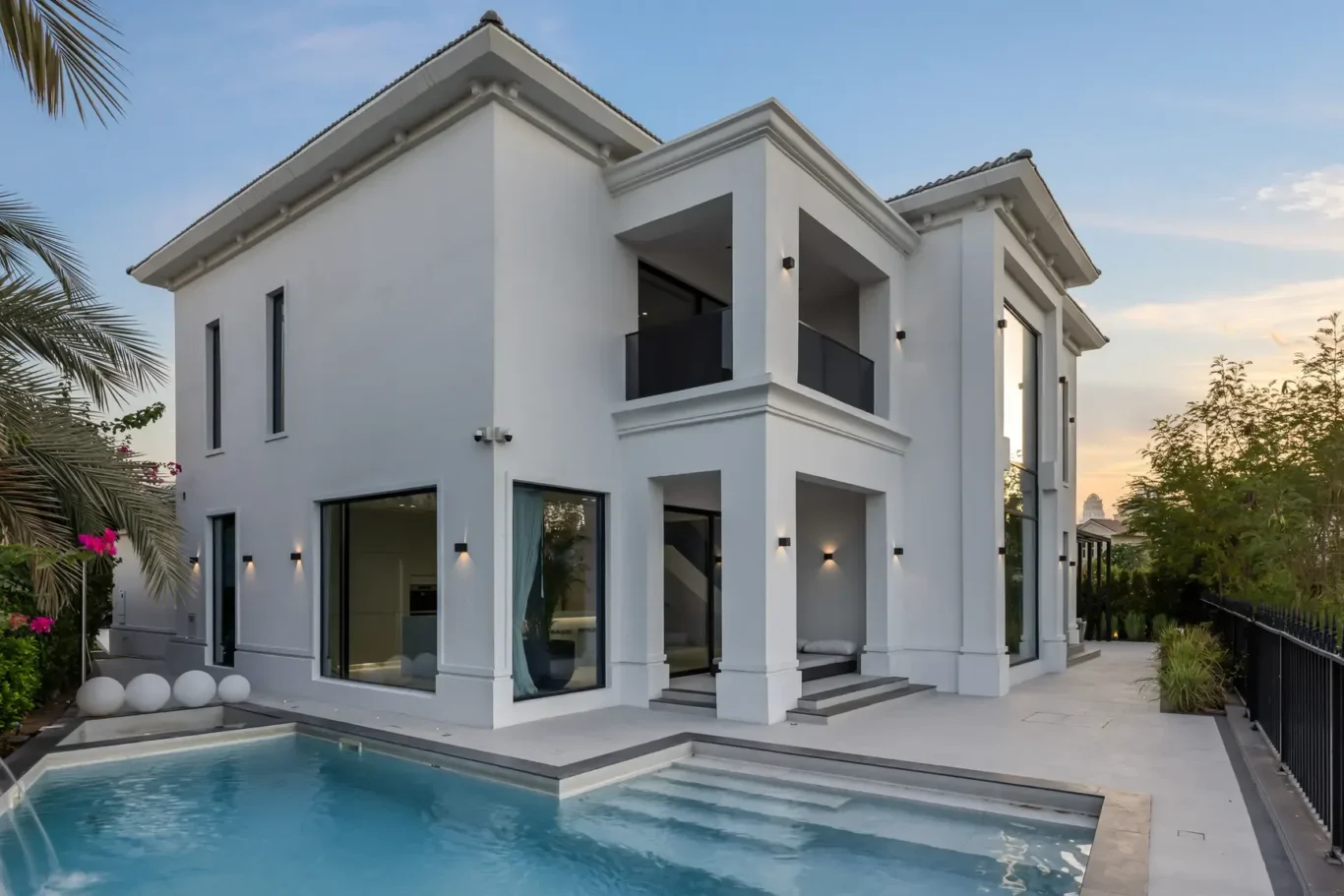 White modern two-story house with large glass doors, balconies, and a rectangular pool in the foreground.