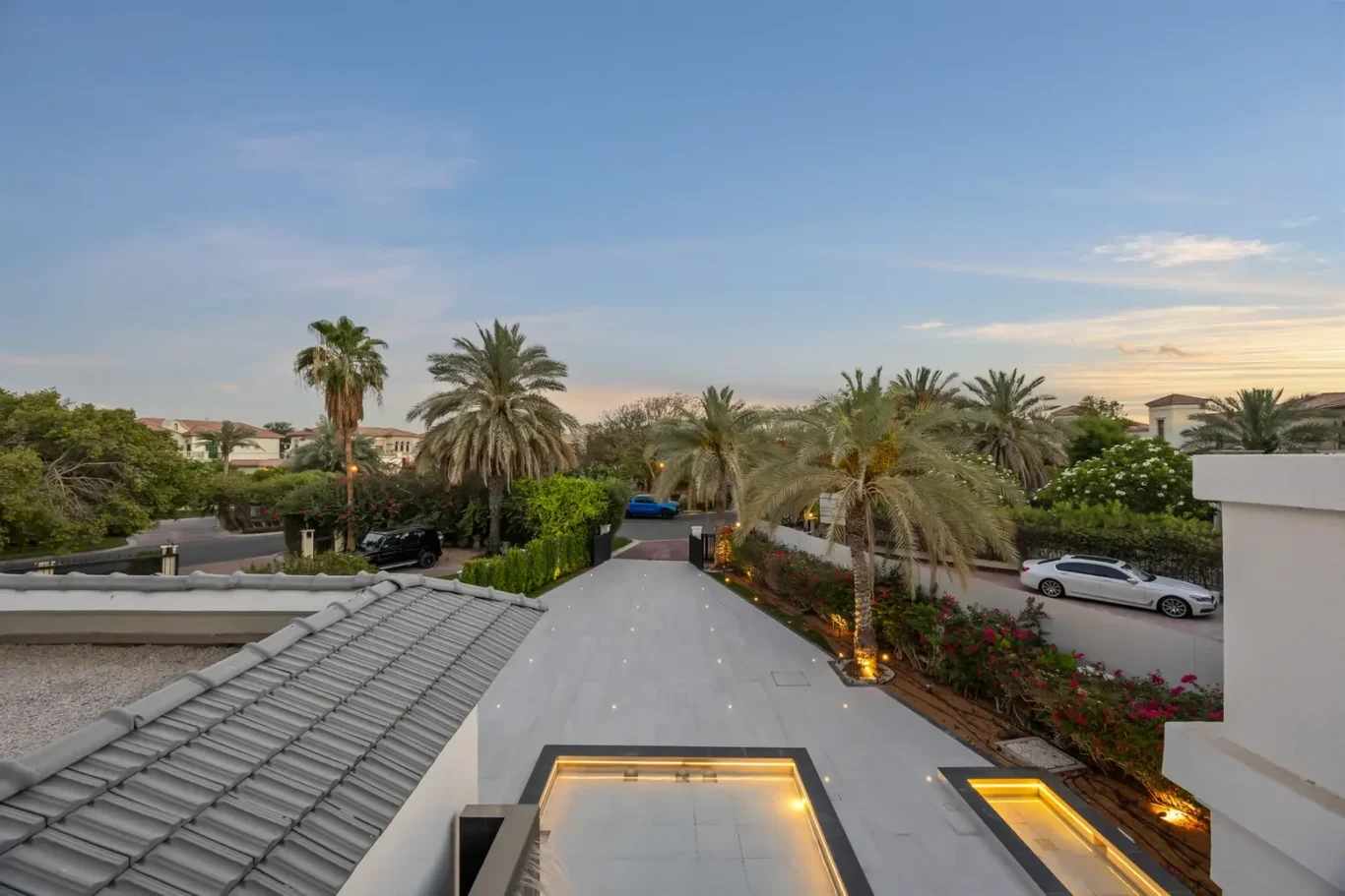 Overhead view of a modern villa complex with a tiled roof, glass skylights, and a palm-lined courtyard at dusk.