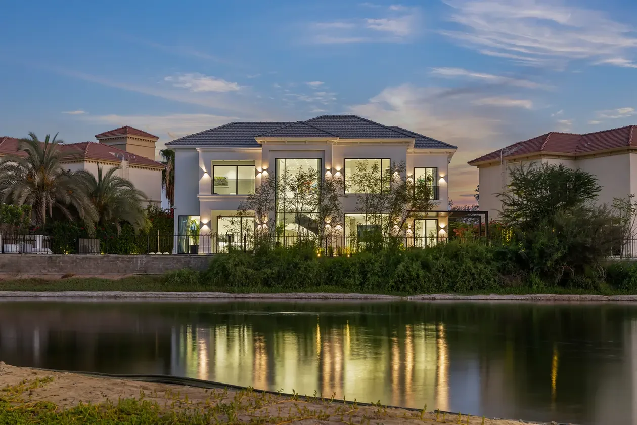 Modern two‑story house with large windows by a canal, lit at dusk, reflecting on the water