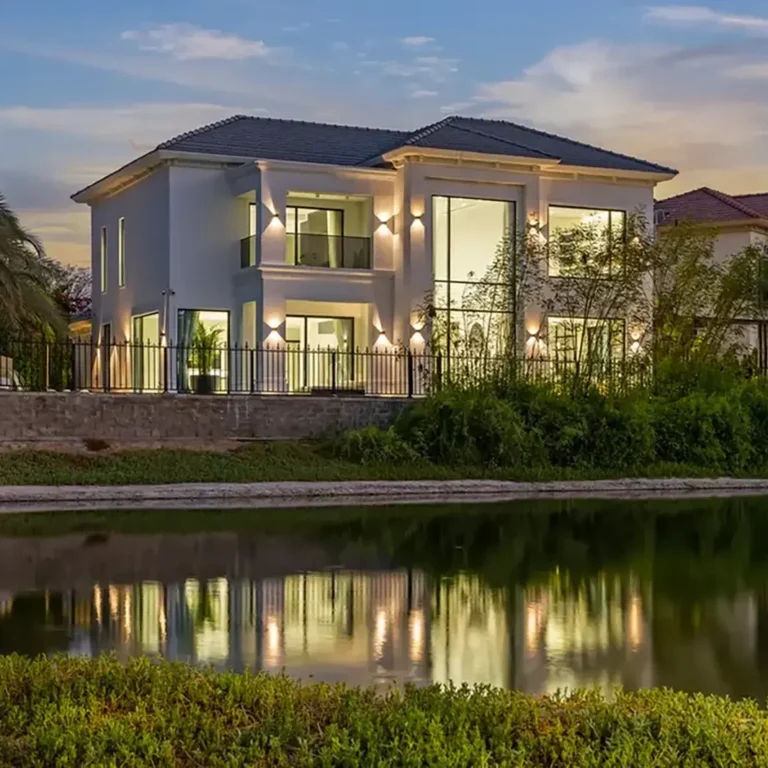 Modern two‑story white house along a canal, lit at dusk with a reflective water surface.