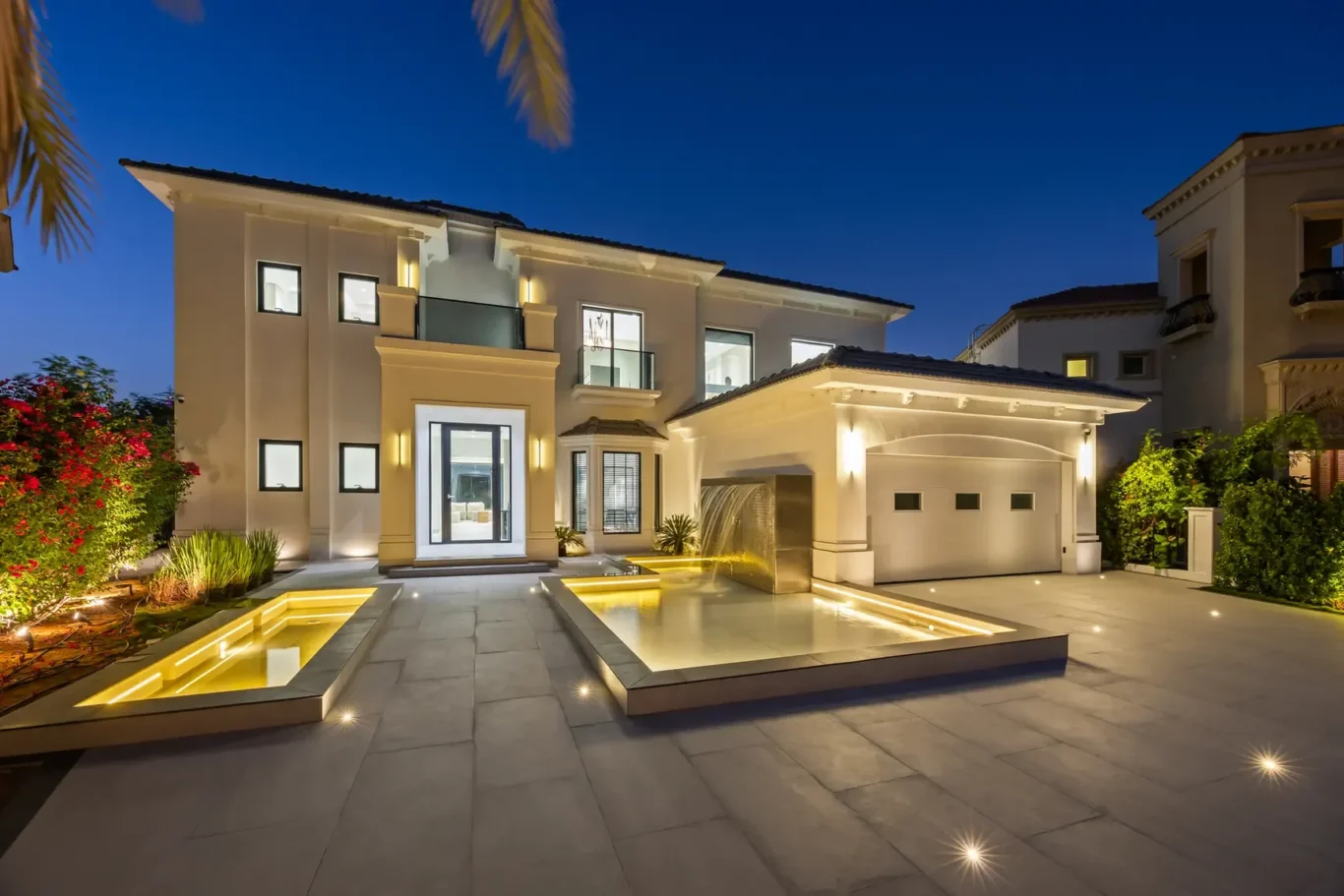 Luxurious modern two-story house at night with illuminated facade and geometric water features in front yard