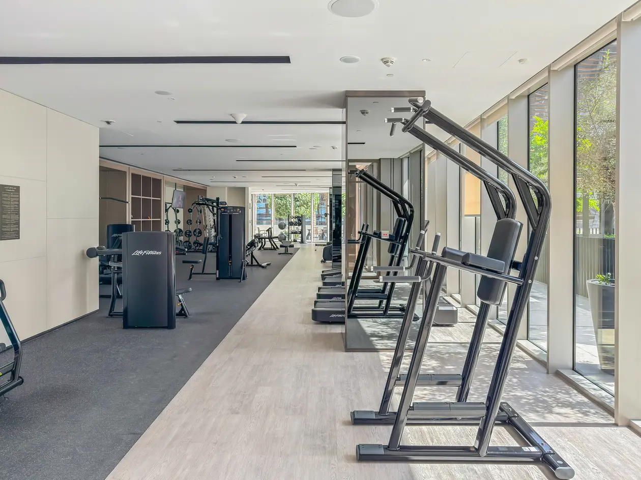 Bright modern gym with multiple treadmills along floor-to-ceiling windows and cardio equipment in the background, daylight streaming in.]','