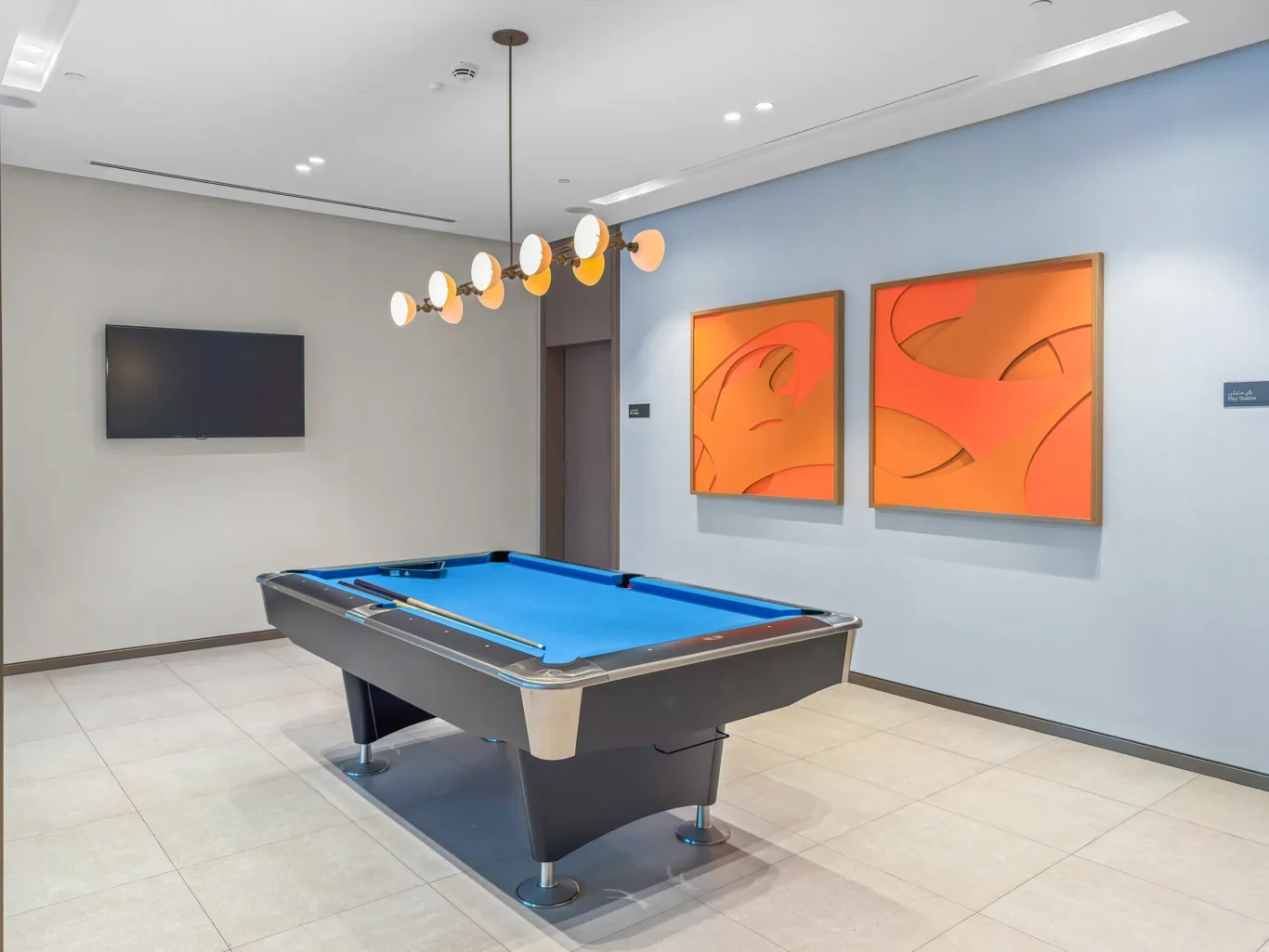 Modern billiards room with blue-felt pool table, cues resting on the table, and a contemporary hanging light fixture with globe bulbs above.