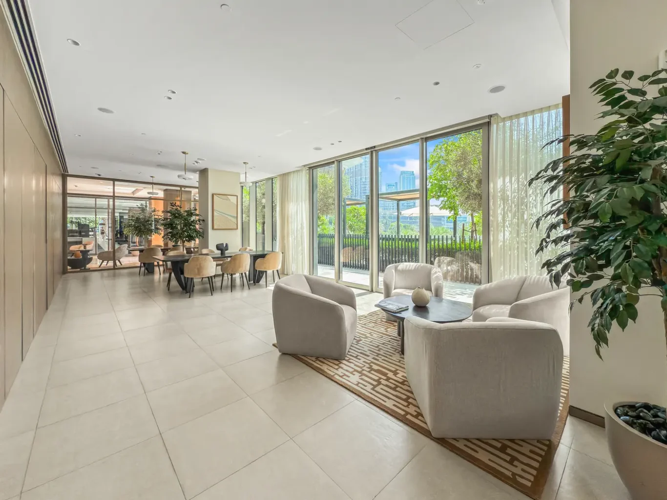 Bright hotel lobby with beige sofas and a glass wall, letting in natural light and greenery outside.