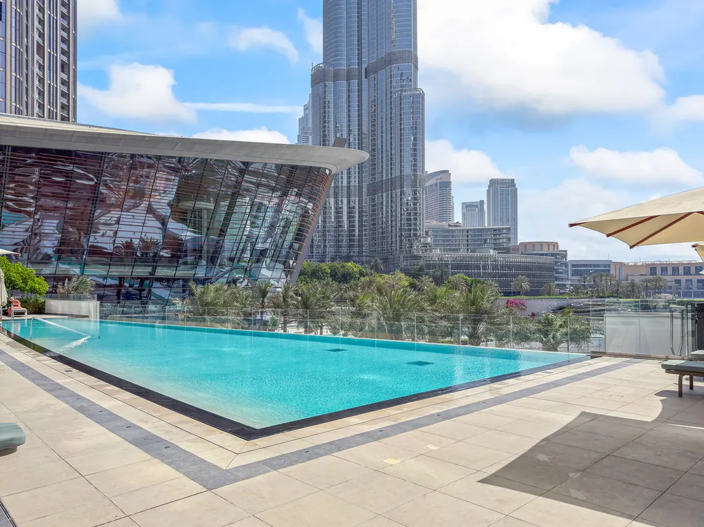 Rooftop swimming pool with clear blue water and a modern glass building, city skyline in the background