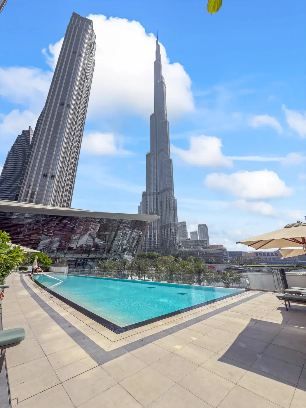 Rooftop pool with sun loungers and umbrellas, overlooking Dubai’s skyline with the Burj Khalifa on a bright, clear day.