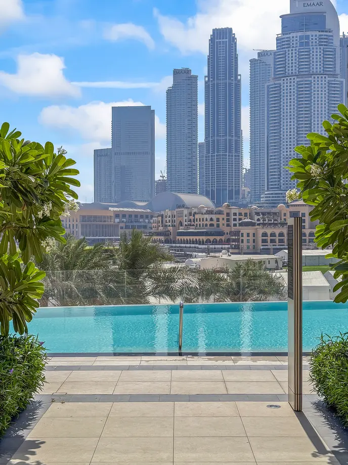 Poolside terrace with a turquoise pool and a cluster of modern skyscrapers in the distance.