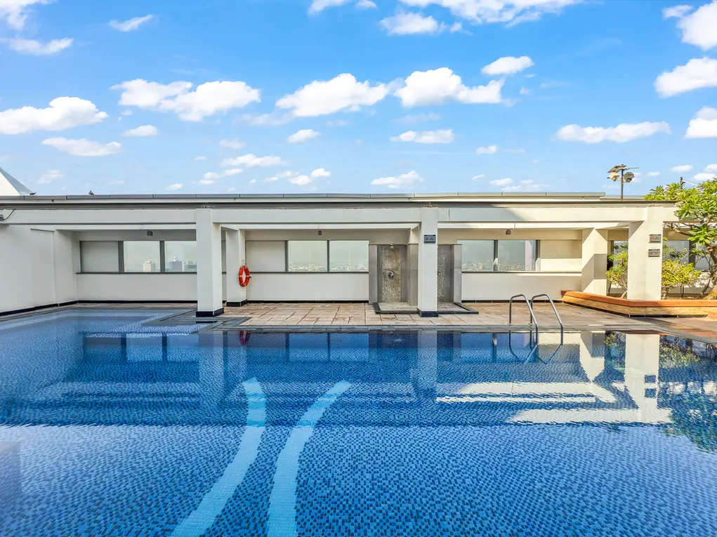 Rooftop swimming pool with blue mosaic tiles, white concrete building, and a clear blue sky.