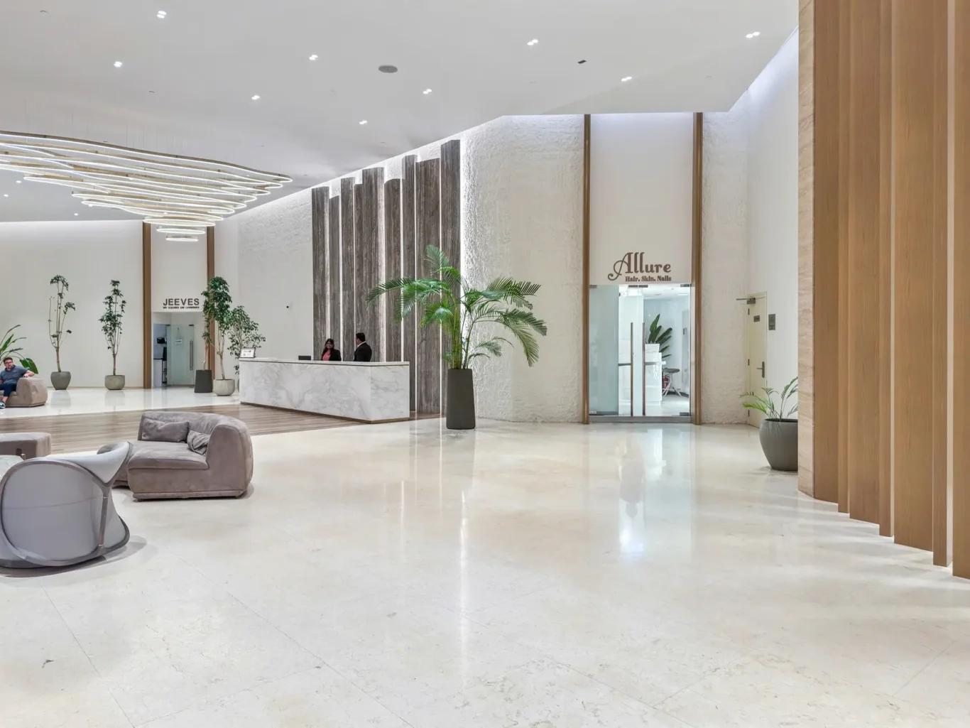 Luxurious hotel lobby with a marble reception desk, tall wooden columns, and large potted plants under circular pendant lights.
