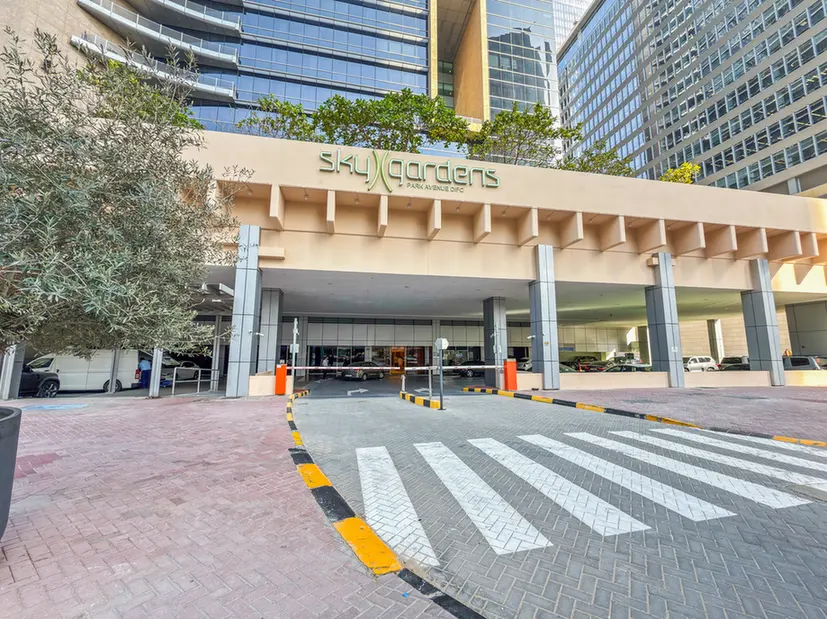 Entrance to SkyGardens building with a covered drop-off area, bold crosswalk stripes, and surrounding tall glass towers.