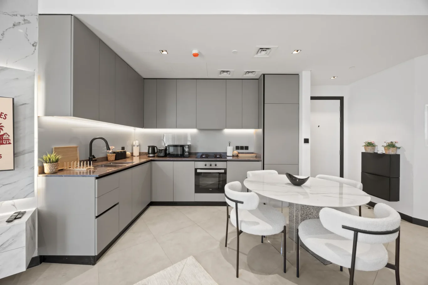 Modern Grey kitchen with wall-to-wall cabinets, marble-topped island, and a round marble dining table with white cushioned chairs.