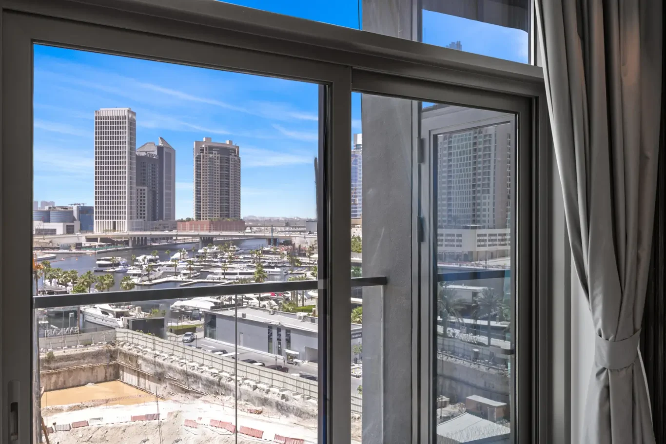 View of a marina and city skyline through a large glass window, with blue sky and tall buildings beyond.