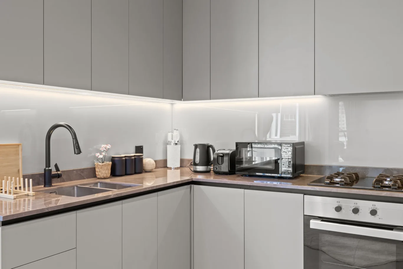 Modern grey kitchen with under-cabinet lighting, sink, and countertop appliances (kettle, toaster, microwave).