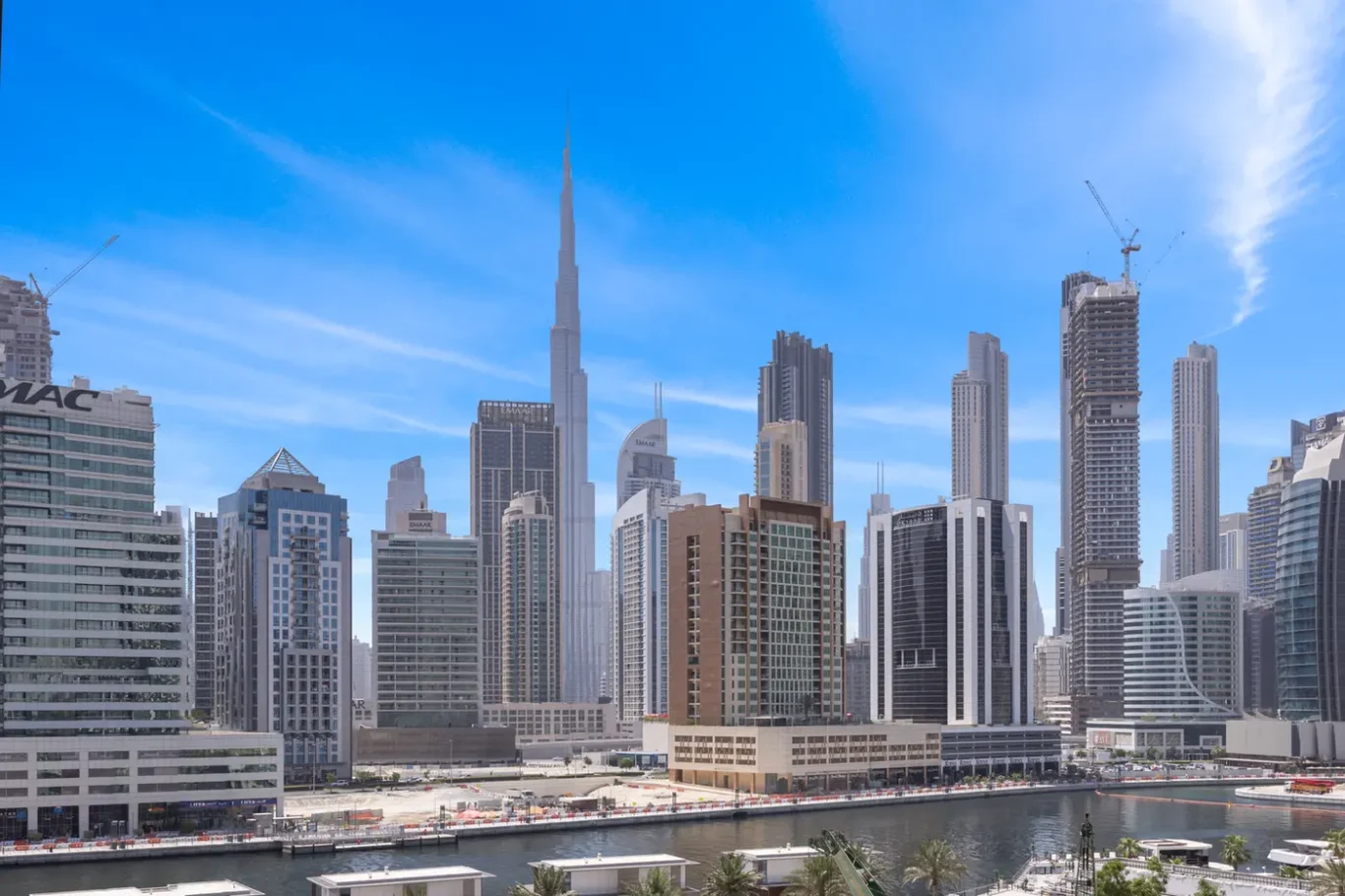 Dubai skyline featuring Burj Khalifa and skyscrapers along a marina under a bright blue sky.
