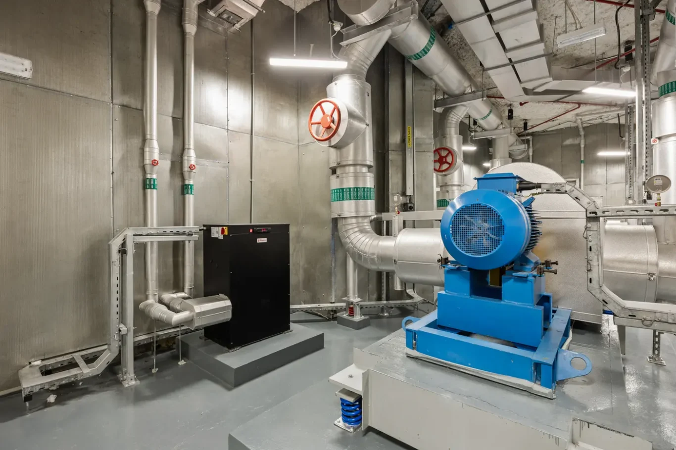 Industrial mechanical room featuring a large blue industrial blower, silver ductwork, and piping.