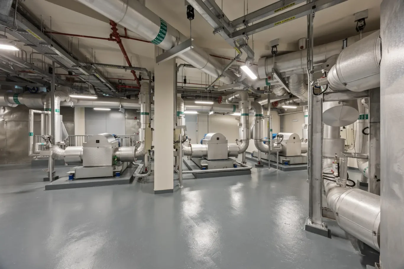 Industrial mechanical room with large silver HVAC ducts, pipes, and machinery on a polished concrete floor
