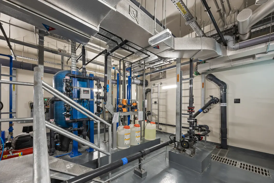 Industrial mechanical room with a large blue tank, pumps, and an array of metal pipes and valves.