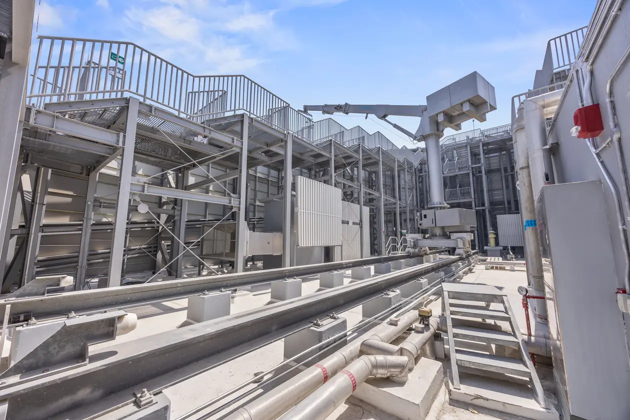 Outdoor industrial facility with steel catwalks, staircases, and large pipelines against a blue sky.