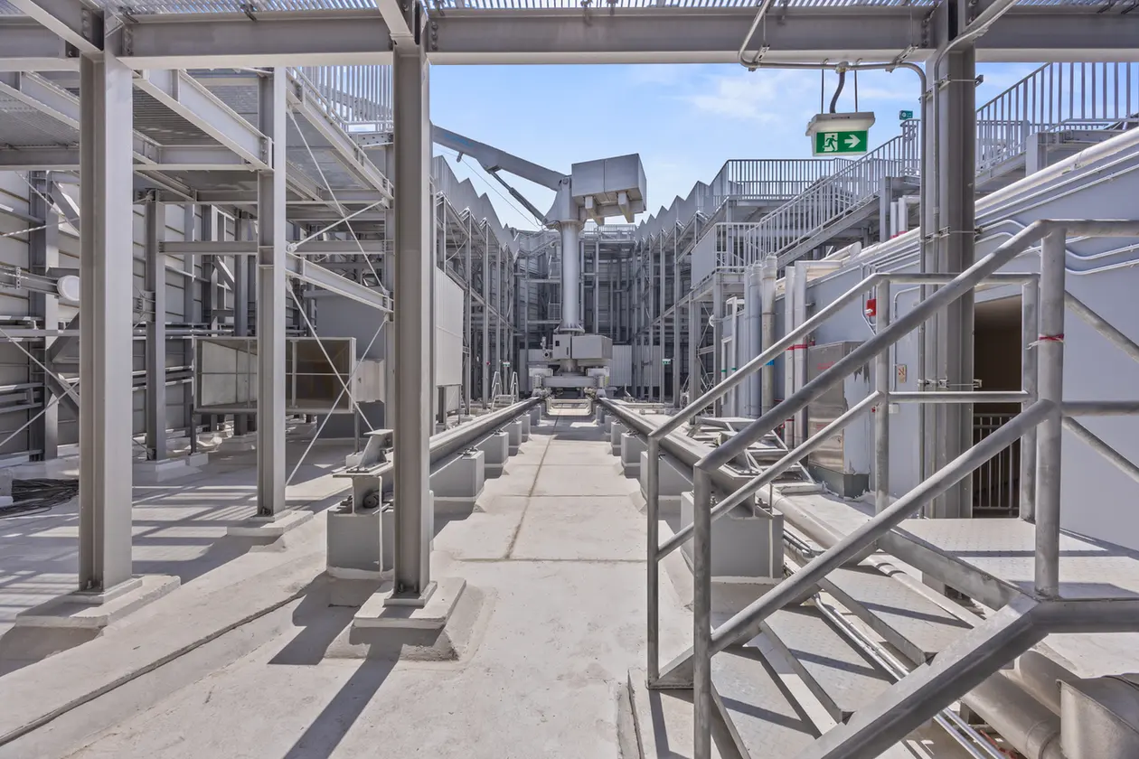 Industrial rooftop with metal walkways, stairs, and machinery under a blue sky, surrounded by steel beams and platforms.