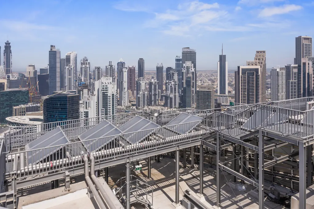 City skyline with tall skyscrapers as seen from a rooftop with metal walkways and railings far in the foreground.