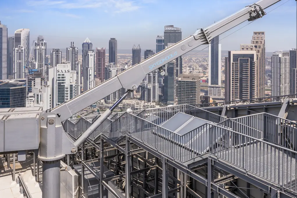 Industrial crane arm extends over a rooftop with a dense city skyline of tall office buildings in the background.