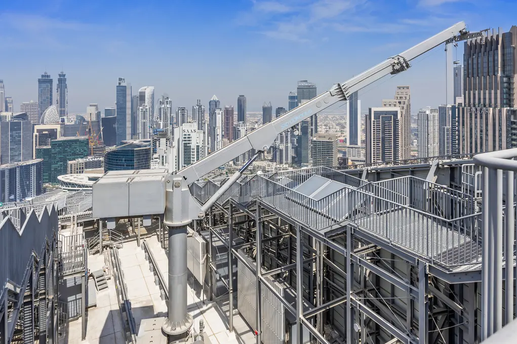 Rooftop construction crane stretching over a dense city skyline of tall glass buildings on a clear day.