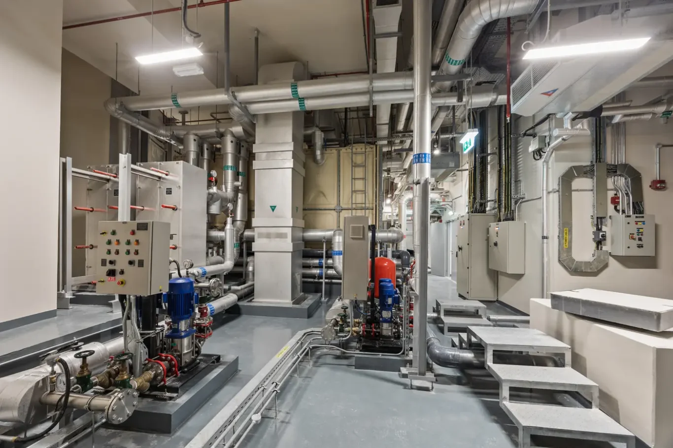 Industrial machinery room with extensive stainless steel piping, valves, and control panels central and foregrounds a blue motor pump