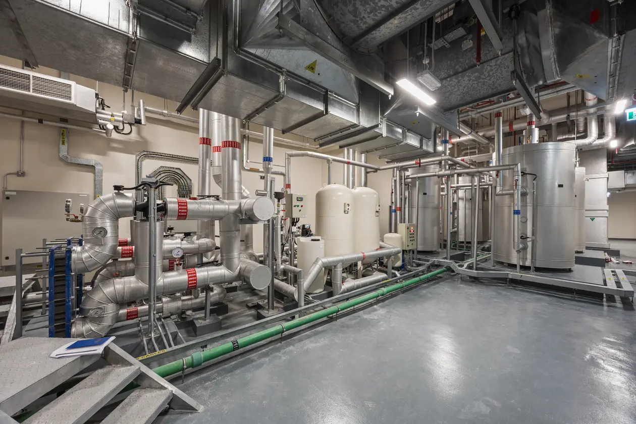 Industrial processing room with silver pipes, tanks, and machinery on a concrete floor