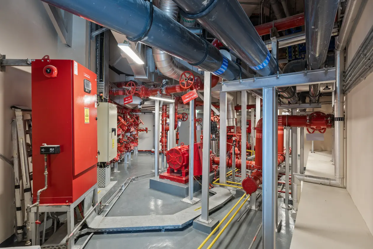 Industrial mechanical room with red pipes, valves, and a large red pump system and control cabinet.