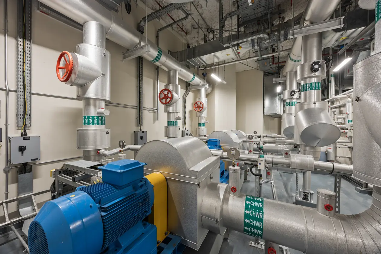 Industrial mechanical room with a large blue motor and extensive silver piping, valves, and gauges.