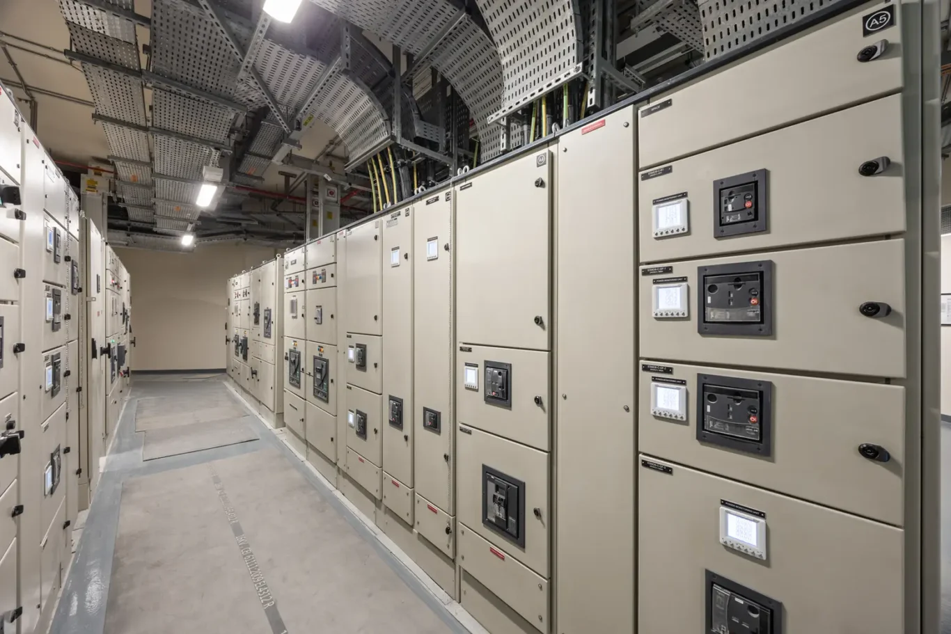Row of large electrical switchgear cabinets in a data center hallway, with cable trays overhead.