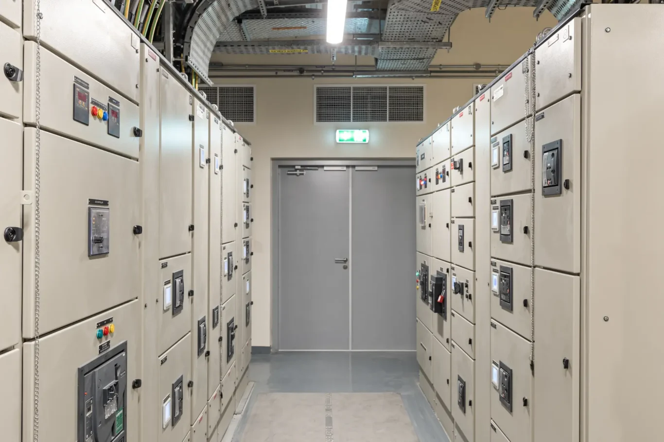 Industrial electrical switchgear room with rows of beige control panels and a central door at back