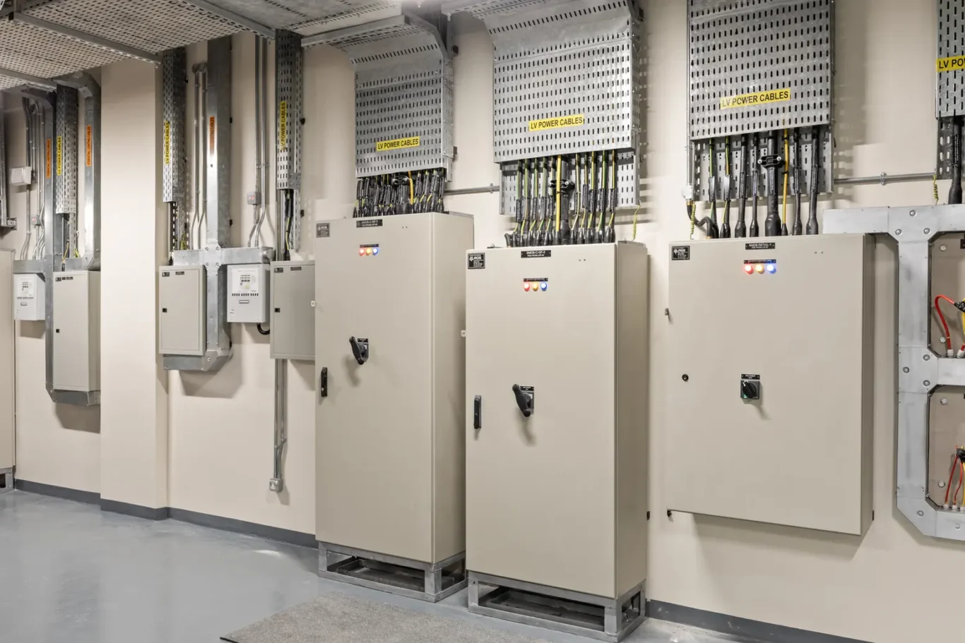 Industrial electrical room with panels, cable trays, and labelled LV power cables along the wall.