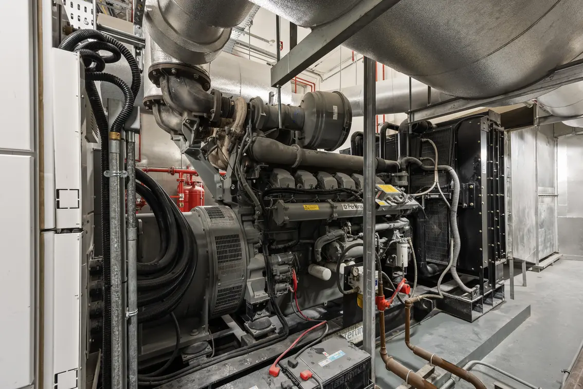 Diesel generator engine in an industrial mechanical room with hoses and metal piping, ready for maintenance.