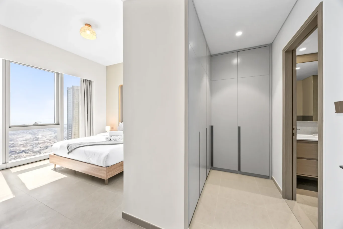 Bright hotel room with a large window showing a cityscape, a low wooden bed, and folded towels on top of it.