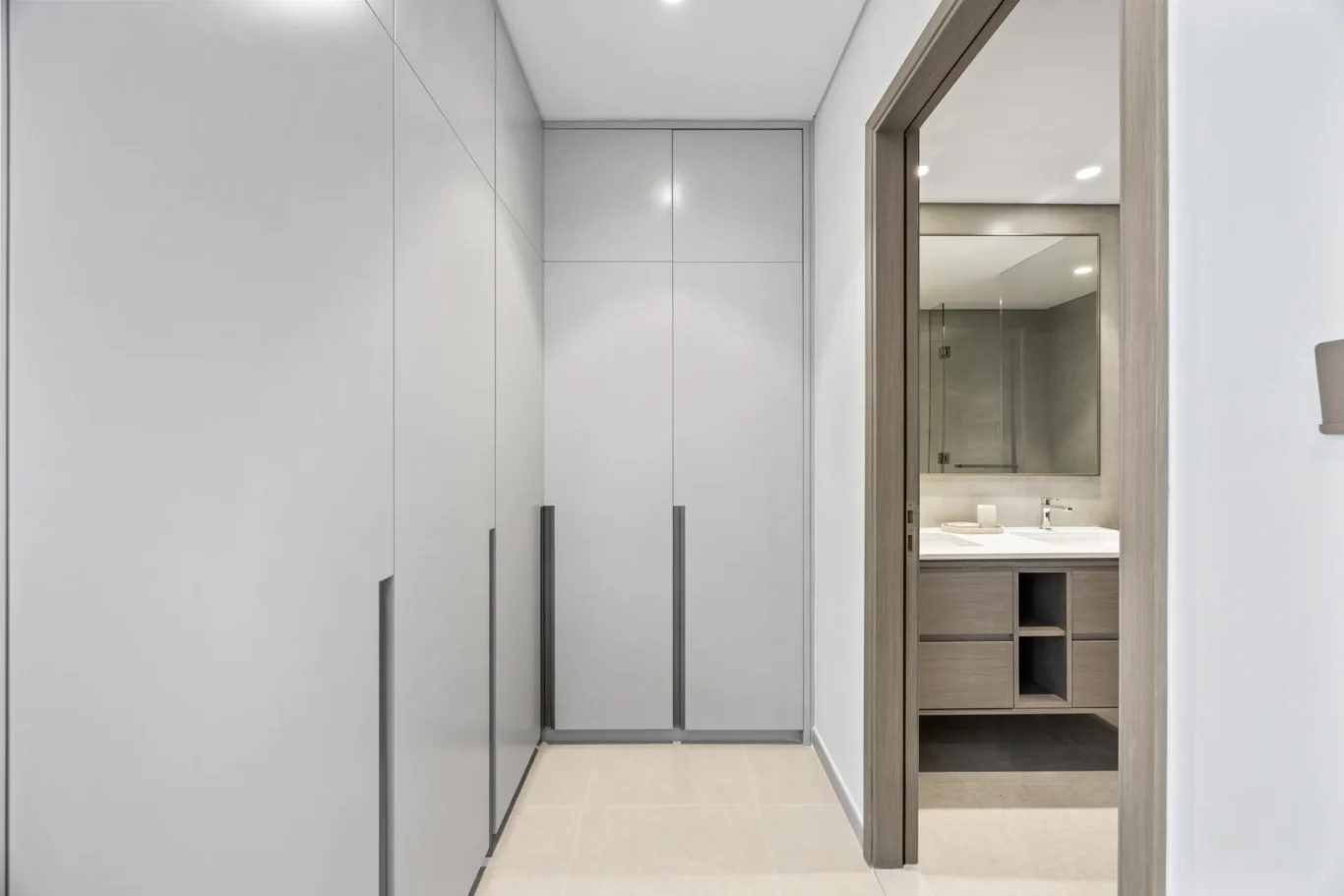 Narrow hallway lined with tall gray built-in cabinets on the left, opening to a bathroom with a wooden-framed doorway on the right.