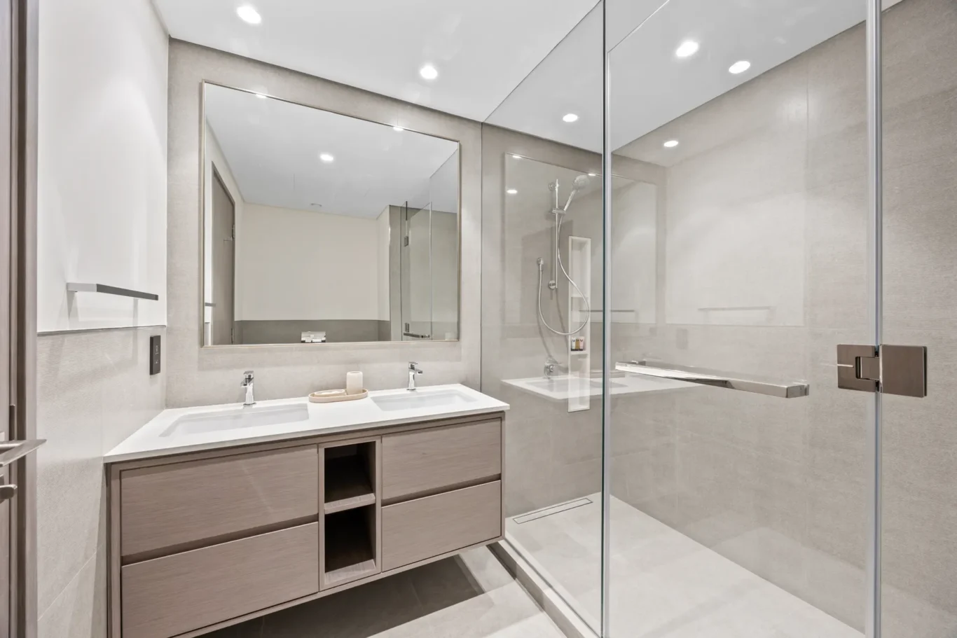 Modern bathroom with dual sinks, wooden vanity, and large mirror reflecting a glass-walled shower area.