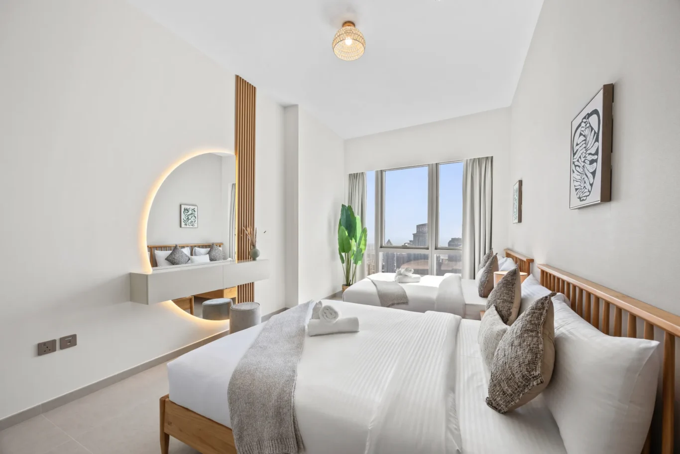 Bright hotel room with two twin beds, white linens, gray throws, and a large window offering city views.
