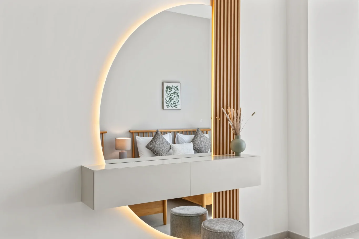 Minimalist bedroom vanity with a circular backlit mirror, white floating dresser, wooden slats, and a bed with gray pillows.