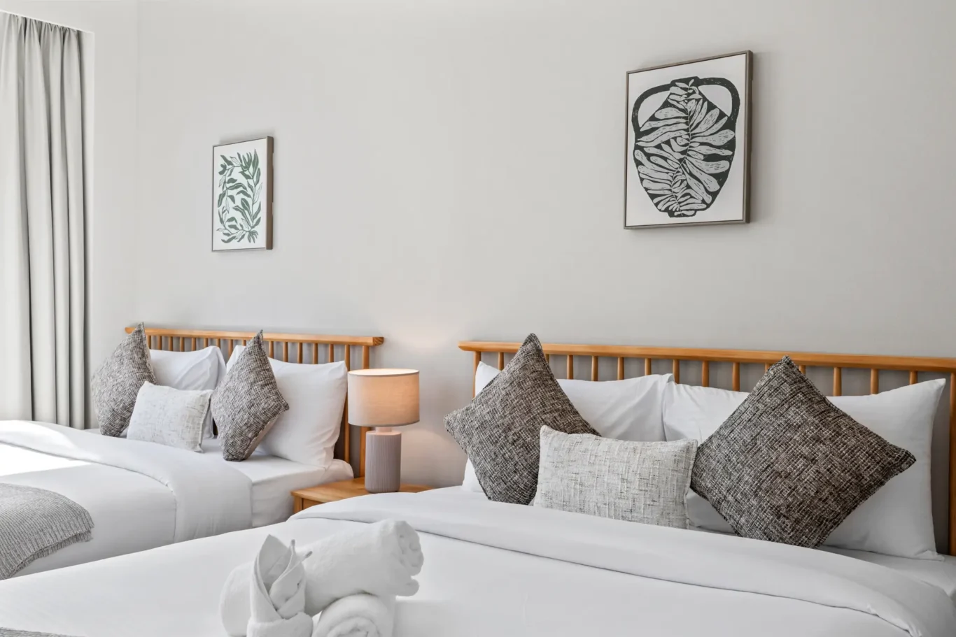 Twin beds with white linens and gray throw pillows in a bright hotel room; framed botanical prints on a light wall above the headboards.