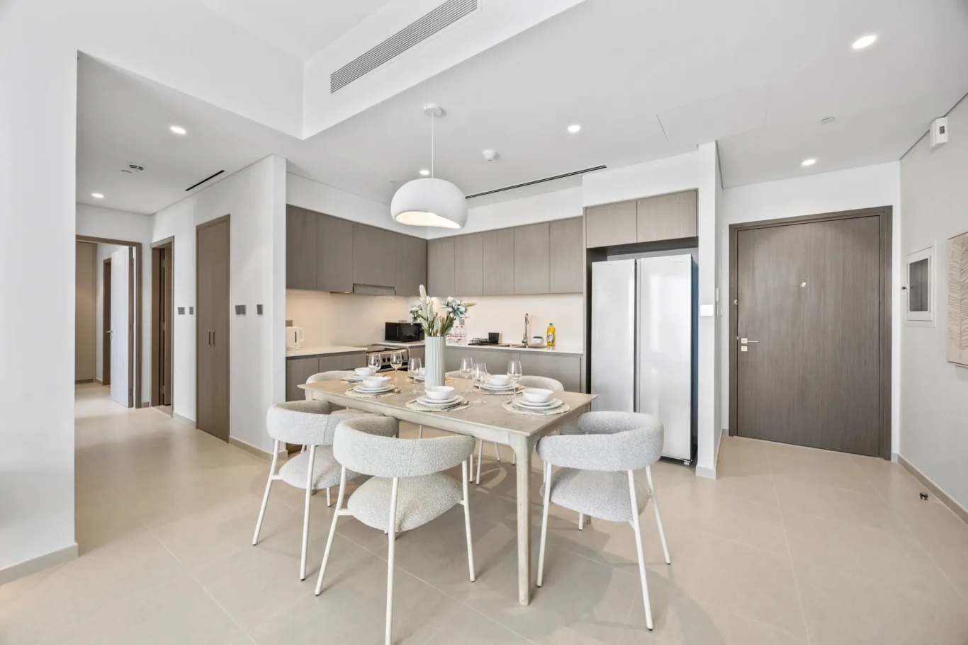 Open-concept kitchen and dining area with gray cabinets, stainless refrigerator, and a wooden dining table set for six.