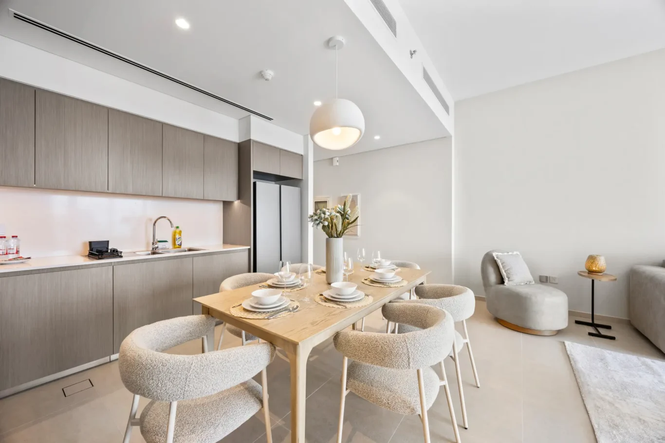 Open-plan kitchen and dining area with gray wood cabinetry, a wooden six-seat table set with bowls and glasses, and a large white globe pendant light.