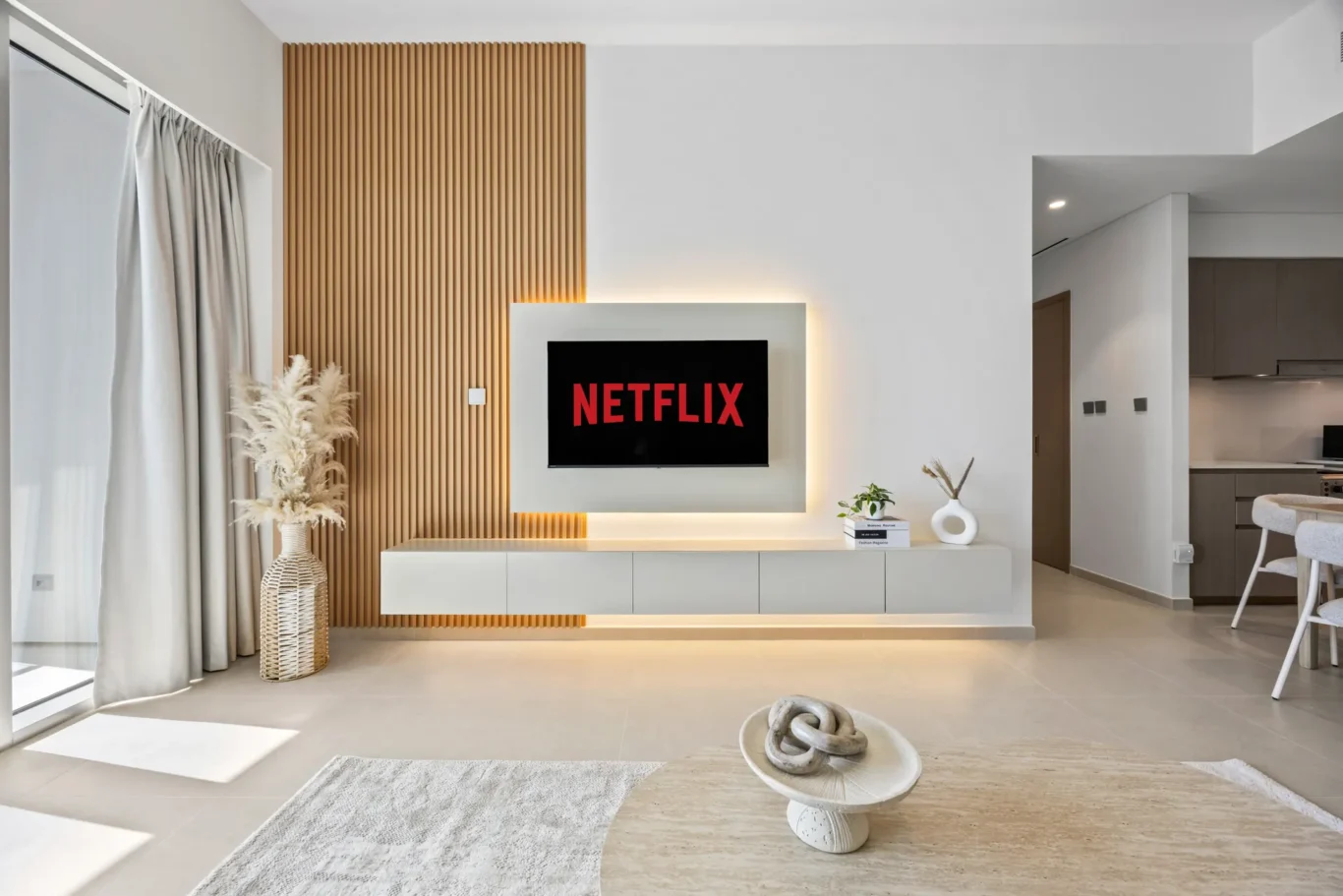 Minimalist living room with a wall-mounted TV displaying Netflix, white console, and a vertical wooden slat accent wall.