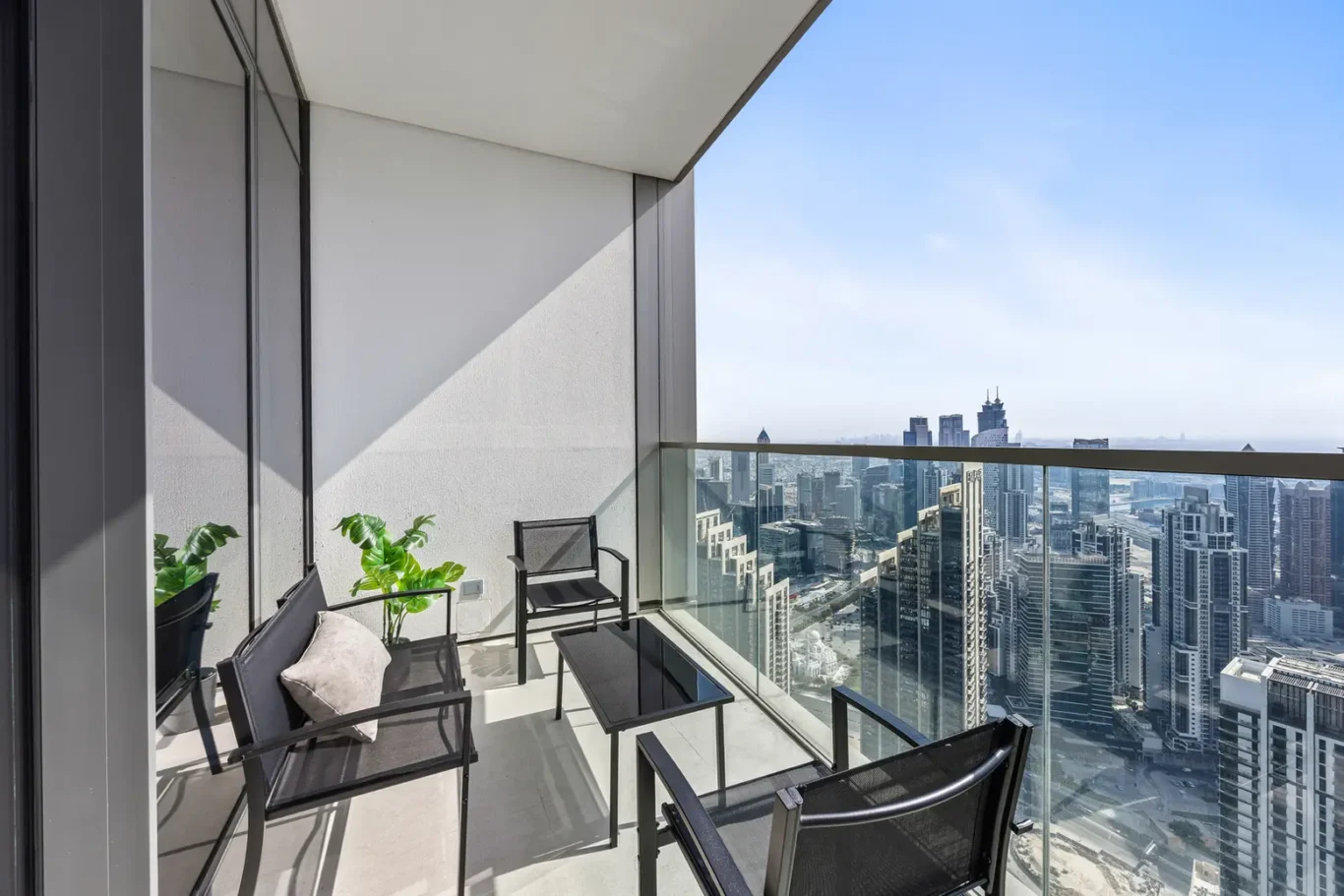 Balcony with black patio chairs and a glass railing overlooking a high-rise city skyline.