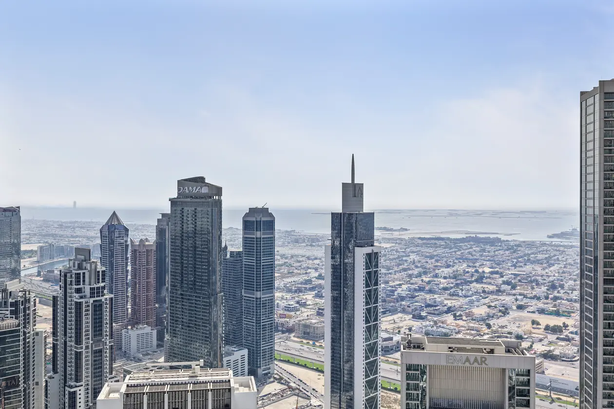 Aerial view of a dense cluster of modern skyscrapers with a distant coastline and water in the background.