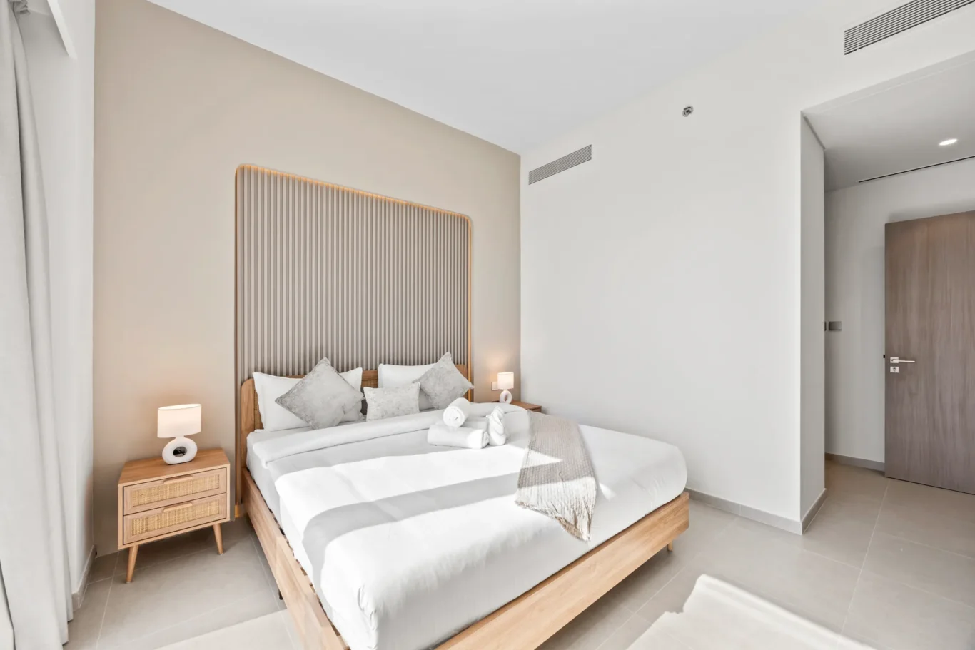 Modern hotel bedroom with a low wooden bed, vertical slat headboard, and beige accent wall