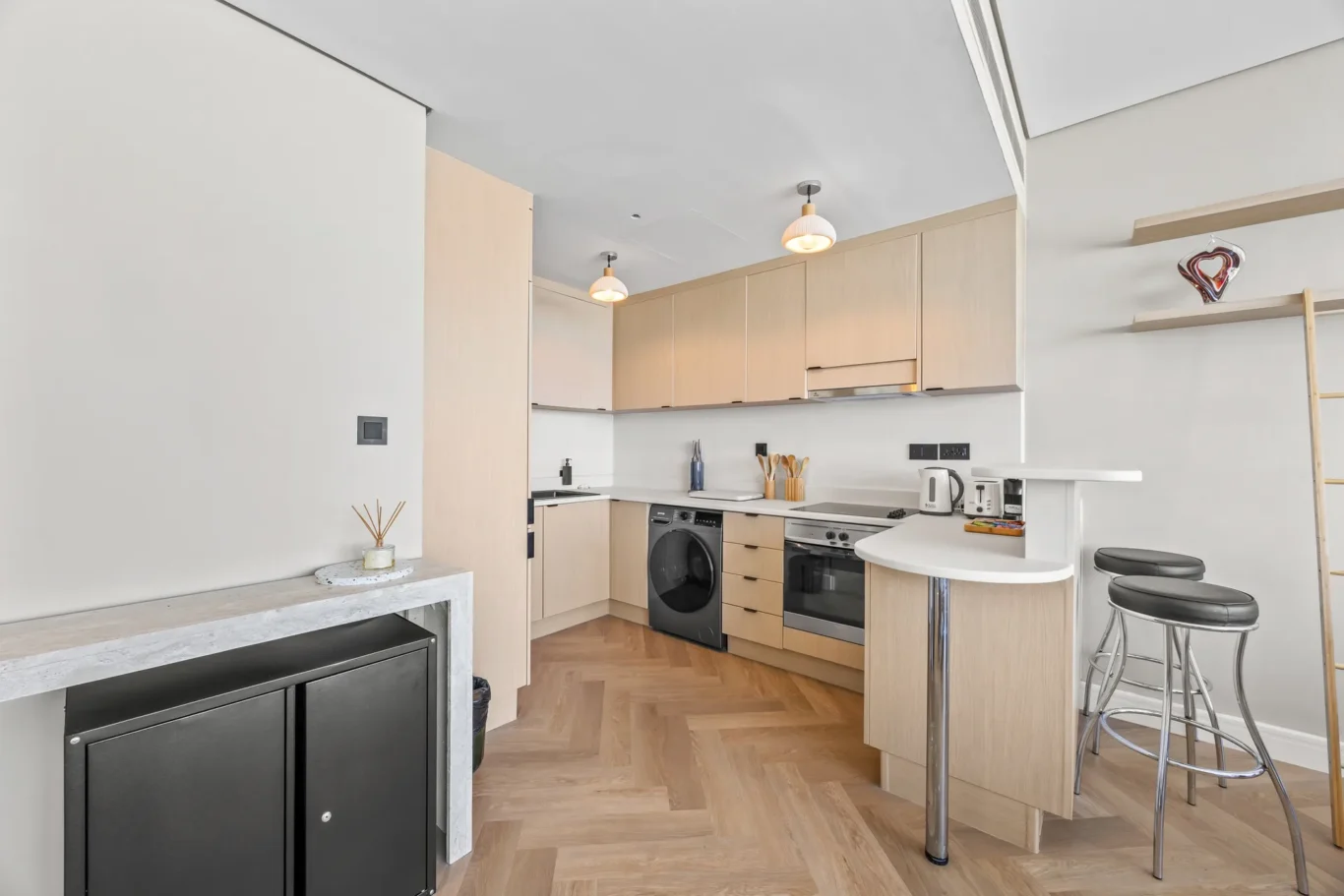 Bright modern kitchen with light wood cabinets, white countertops, and stainless-steel appliances.
